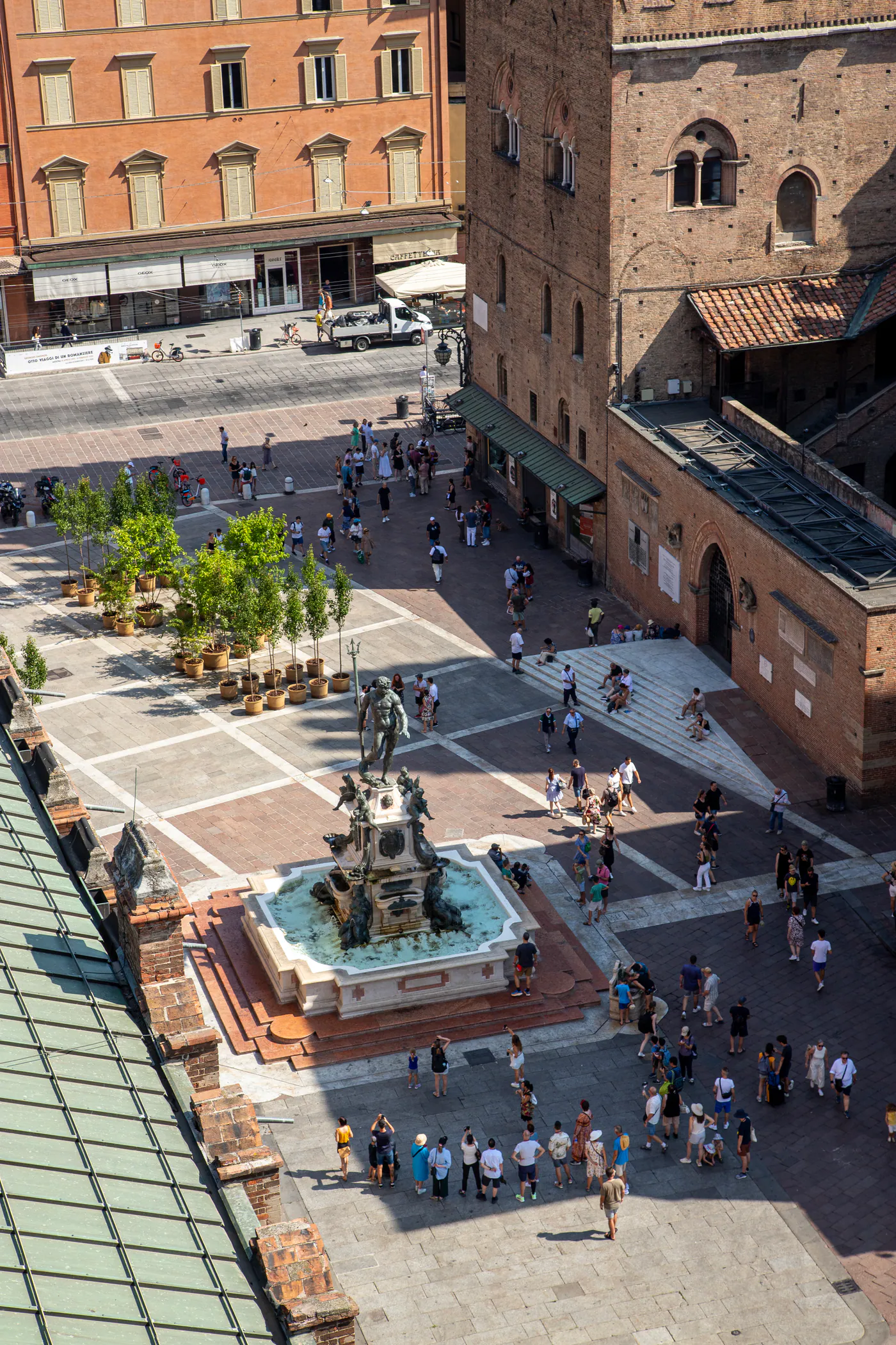 Blick von oben auf einen Platz mit einem Brunnen samt Statue, viele Menschen, Backsteingebäude und ein Turm